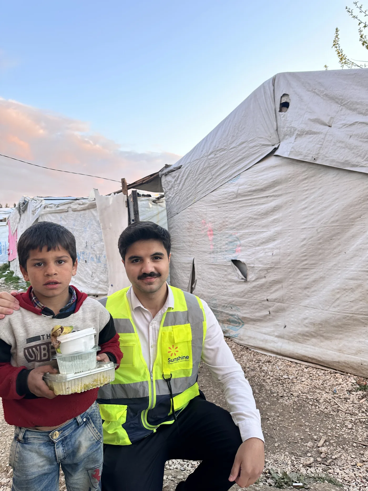 Sunshine-Aid-Helfer mit einem Kind vor einem Zelt im Lager